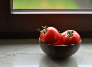 Vibrant red tomatoes in a rustic wooden bowl placed by a sunny window, perfect for illustrating organic freshness.